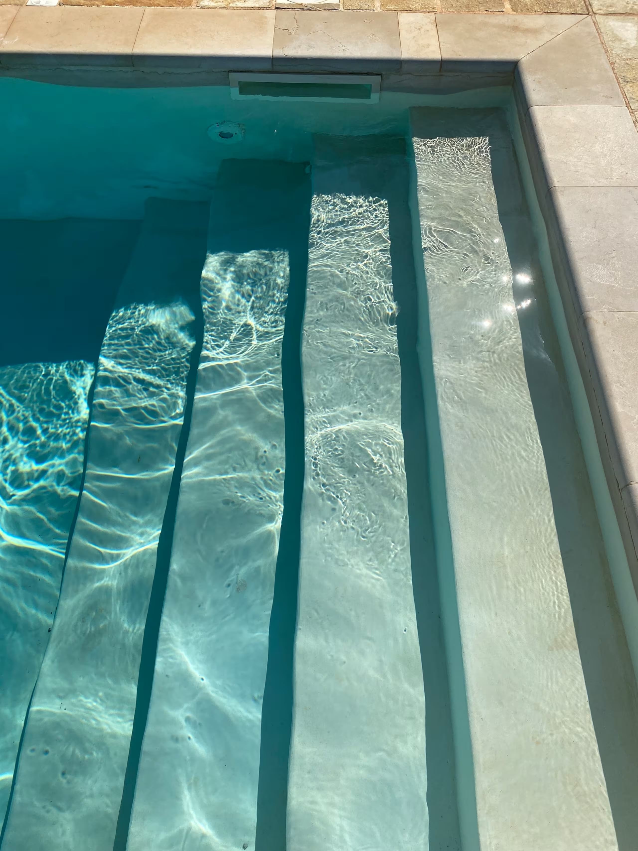 Sunlit steps descending into the turquoise pool at Trullo dei Pini, edged in pale stone